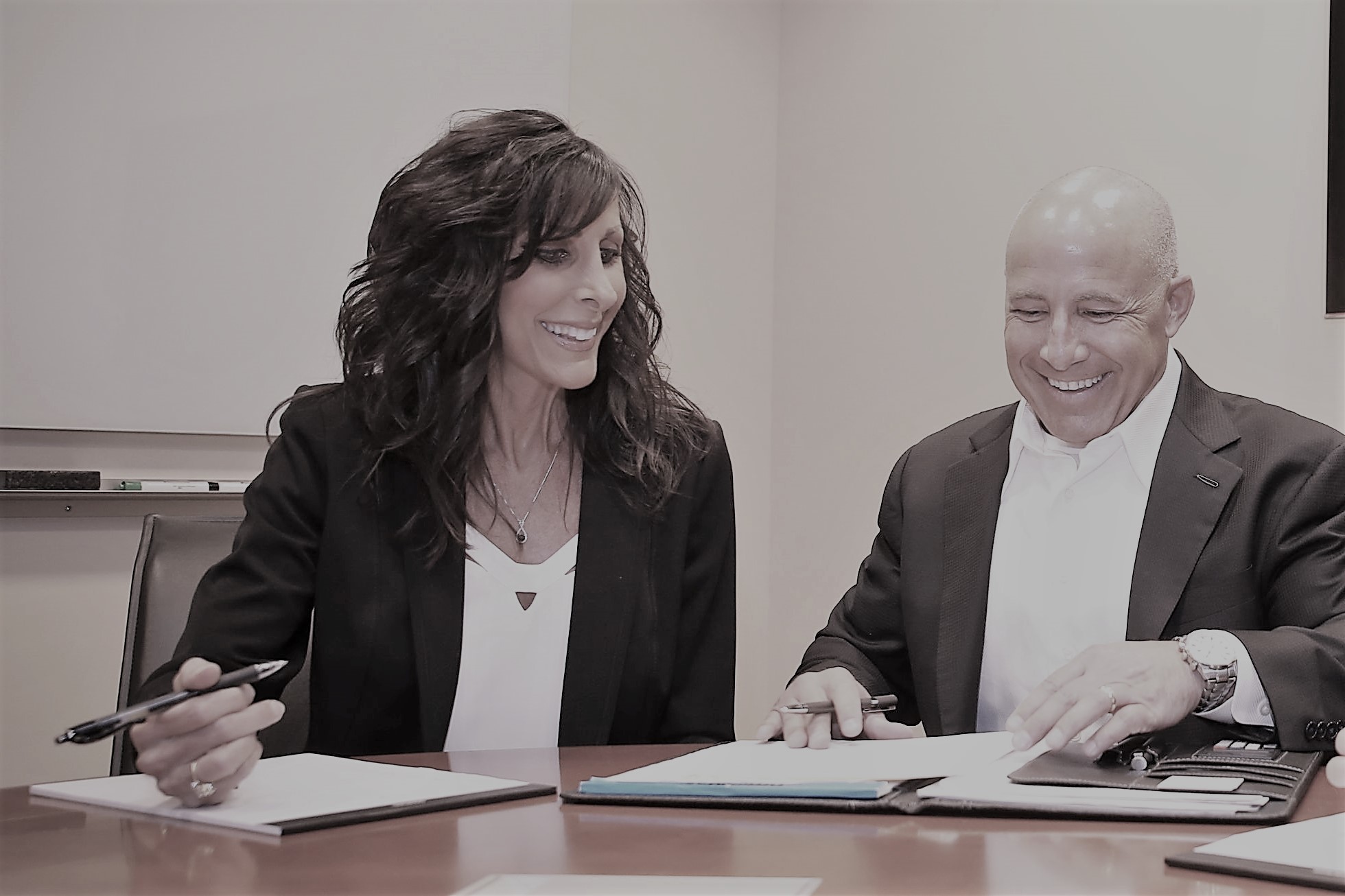 Two people sitting at a table with papers and pens.